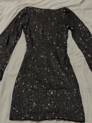 Meet Me There glittrig miniklänning - Snygg svart kortklänning med långa ärmar och v-ringning på ryggen. Klänningen är täckt av glittriga paljetter som ger en festlig look. Figurnära passform och stretchigt material för extra komfort. Perfekt för dig som vill sticka ut. Klänningen e ganska kort i längden men ör fortfarande lika snygg!