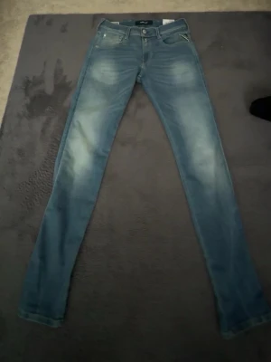 Blå slim fit jeans från Replay - Snygga blå slim fit jeans från Replay med klassisk femficksmodell och ljusa slitningar framtill. Jeansen har normal midja, raka ben och är tillverkade i mjuk denim med stretch för extra komfort. Perfekta för en avslappnad och trendig look. Det är ett par helt oanvända jeans har testat de en gång men de passade inte mig, bara att skriva till mig om ni har funderingar/frågor 