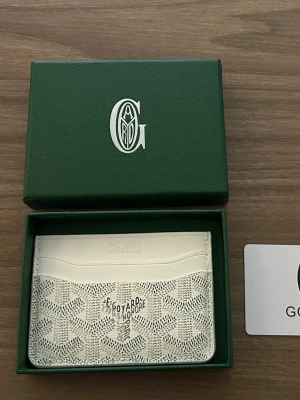 Vit korthållare med mönster - Snygg vit korthållare i läder med diskret mönster i grått och svart. Kommer i en grön ask och har flera fack för kort. Perfekt för dig som vill ha en stilren och praktisk accessoar i fickan.