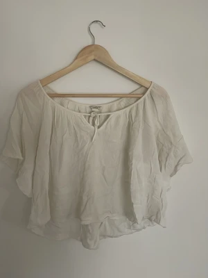 Vit flowy blus - Säljer en vit, flowy blus med korta ärmar och rund halsringning med liten knytning fram. Blusen har en avslappnad passform och är gjord i ett tunt tyg som ger en bohemisk känsla. Perfekt för sommaren❣️