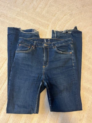 Blå bootcut jeans med hög midja - Säljer ett par klassiska blå bootcut jeans med hög midja och femficksmodell. Jeansen har en snygg mörkblå tvätt och lätt utsvängda ben. Perfekta för dig som gillar en tidlös och trendig look.