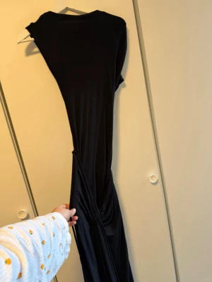 Svart långklänning med snörning - Svart långklänning i mjukt och följsamt material med snygg snörningsdetalj i midjan. Klänningen har ärmlös design och en stilren, enkel look som passar perfekt när du vill känna dig extra snygg.