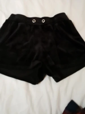 Svarta velourshorts från Gina Tricot - Mysiga svarta shorts i mjuk velour från Gina Tricot. De har resår i midjan med två metallöljetter framtill för snörning. Perfekta för en avslappnad och chill stil.