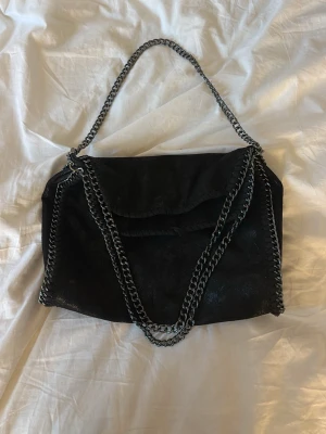 Svart efterliknande stella McCartney handväska - Cool svart handväska Temu med kedjedetaljer i silver runt kanterna och som axelrem. Väskan har en mjuk, lite glansig yta och klassisk flap-stängning.