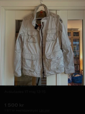Parajumpers windbreaker dessert woman - Snygg ljusgrå vindjacka från Parajumpers med flera praktiska fickor framtill, hög krage och dragkedja. Jackan har en klassisk patch på ärmen och är tillverkad i ett lätt, vindtätt material. Perfekt för dig som vill ha en stilren och funktionell jacka.