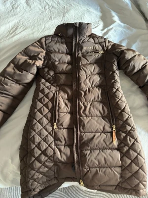 Jackson Mary jr jacka  - Snygg brun lång dunjacka från Jackson , jätte skön och använd en vinter. Bråkig dragkedja som behöver bytas därav priset! Finns luva till