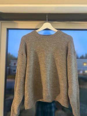 Beige stickad tröja med rund hals - En enkel och stilren beige stickad tröja med rund halsringning och långa ärmar. Tröjan har ribbstickade muddar vid hals, ärmslut och nederkant. Perfekt för lager-på-lager och passar till det mesta.