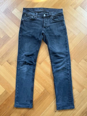 Svarta Nudie Grim Tim jeans - Snygga svarta/mörkgråa Grim Tim jeans från Nudie Jeans med klassisk femficksdesign. Storleken är W28 L30. Hör av dig vid minsta fundering!