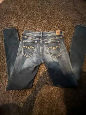 Blå slim fit jeans från Replay - Snygga blå slim fit jeans från Replay med klassisk femficksdesign och gulddetaljer på bakfickorna. Jeansen har en lätt tvättad look och smala ben. Perfekta för dig som gillar en modern och avslappnad stil. Storlek W28 L32