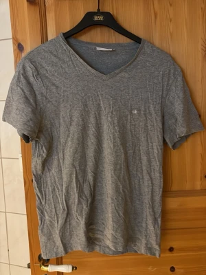 Grå v-ringad t-shirt från Calvin Klein - Grå t-shirt från Calvin Klein med v-ringning och liten CK-logga på bröstet. Klassisk passform och korta ärmar, tillverkad i mjuk bomull. Perfekt för en avslappnad och stilren look.