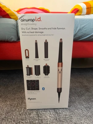 Dyson Airwrap i.d. stylingverktyg - Multifunktionellt stylingverktyg från Dyson i beige och koppar med flera tillbehör för att torka, locka, forma och släta ut håret utan värmeskador. Inkluderar olika borsthuvuden och cylindrar för styling av rakt och vågigt hår. Bluetooth-funktion för personliga inställningar.