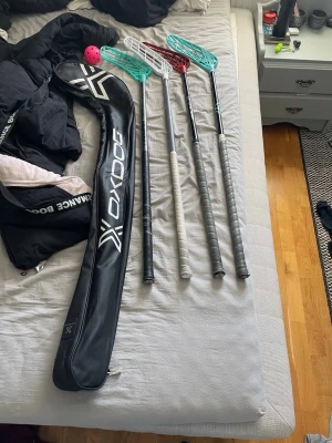 Innebandyklubbor och väska Oxdog - Fyra innebandyklubbor och en oxdog väska för klubborna. Bild två ser man de bättre och dyrare klubborna, den med blått blad har knappt använts och den med rött blad har jag använt som mest. På den röda har jag bytt blad från blå till röd, har inte kvar bladet. Både klubborna har fått nya klubbhuset lindor som är lite använda. På bild tre visar jag att salming klubbans linda är vit och är lite smutsig och kanske måste bytas. Den klubban på sista bilden har ett märke på skaftet där nere.storlek ?