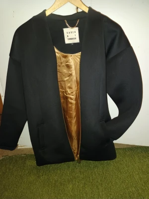 Svart minimalistisk jacka från Karen by Simonsen - Elegant svart jacka med guldig insida och rena detaljer. Stilren och lätt att matcha till både vardag och finare outfit. Oversized/modern passform. Bra skick.