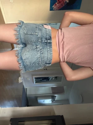 Blå jeansshorts med fransar - Säljer ett par ljusblå jeansshorts från Bik Bok med fransiga kanter och klassiska bakfickor. Shortsen har en hög midja och är perfekta för varma sommardagar. Snygg och avslappnad stil som passar till allt.