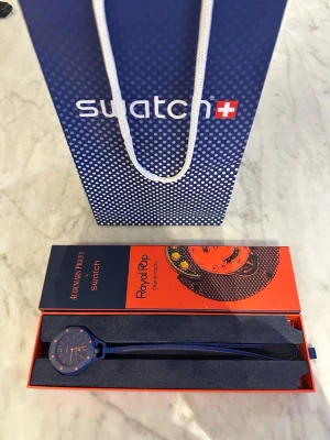  Swatch x Audemars Piguet Royal Pop Orenji Hachi  klocka - Säljer en blå Swatch x Audemars Piguet Royal Oak klocka med rund urtavla och orange detaljer. Klockan har ett sportigt och modernt utseende med silikonarmband och cool design på urtavlan. Perfekt för dig som gillar unika accessoarer.