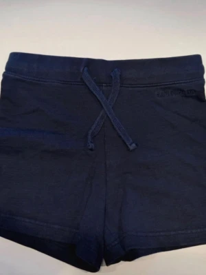 💙 Lexington Shorts 146/152 – Stilrena & Bekväma 💙 - Säljer ett par mörkblå shorts från Lexington i storlek 146/152, köpta från Kids Brand Store. Perfekta till sommaren med både snygg och bekväm passform!  Shortsen har resår och snörning i midjan för optimal komfort samt en ton-i-ton broderad logga på höften som ger en stilren och exklusiv känsla. Den kortare modellen gör dem perfekta för varma dagar och aktiviteter.  ✔ Mjuk och bekväm passform ✔ Resår & snörning i midjan✔ Stilren brodyrdetalj✔ Färg: Dark Blue✔ Kanonskick✔ Djur- och rökfritt hem  
