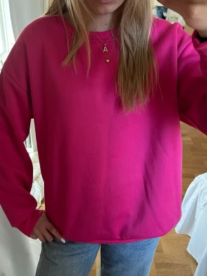 Oversized ceriserosa hoodie - En oversized hoodie i en stark ceriserosa färg. Tröjan har rund halsringning, långa ärmar och ribbade muddar vid ärmslut och nederkant. Perfekt för en chill och avslappnad stil. Materialet känns mjukt och bekvämt mot huden.