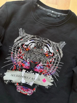 Zavetti sweatshirt - Svart sweatshirt från Alessandro Zavetti med ett stort, färgstarkt tigertryck på framsidan. Tröjan har rund halsringning och ribbade muddar vid ärmslut och nederkant. Storlek M💫