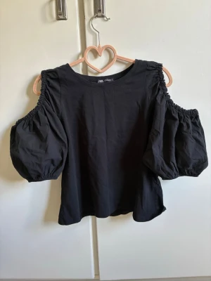 Svart offshoulder topp från Zara - Trendig svart topp från Zara med offshoulder-design och puffiga korta ärmar. Aldrig använd och därmed i nytt skick. Perfekta för skolan och sommaren💗