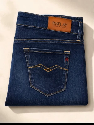 Mörkblå jeans från Replay - Snygga mörkblå jeans från Replay med klassisk femficksmodell och raka ben. Jeansen har kontrastsömmar, läderpatch med logga bak och diskret sliten effekt framtill. Perfekta för dig som gillar stilrena och tidlösa jeans i denim.