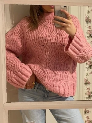 Rosa stickad tröja från H&M - Supermysig rosa stickad tröja från H&M med grovt kabelstickat mönster och hög krage. Tröjan har lång ärm och en loose fit som ger en chill vibe. Perfekt för kalla dagar! Köpt på Sellpy i nyskick