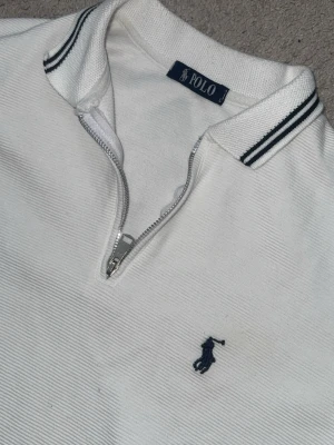  Ralph Lauren - Vit polotopp från Polo Ralph Lauren med klassisk krage och halv dragkedja framtill. Broderad marinblå logga på bröstet och diskreta ränder på kragen. Perfekt för en stilren look. Köpt för 1000kr . Pris kan diskuteras 