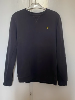 Svart sweatshirt från Lyle & Scott - Klassisk svart sweatshirt från Lyle & Scott med rund halsringning och den ikoniska gula loggan broderad på bröstet. Tröjan har långa ärmar och ribbade muddar vid ärmslut och nederkant. Perfekt för en avslappnad och stilren look. Storlek S/14-15år. Pris kan diskuteras vid snabb affär!