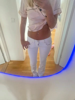 Vita low waist jeans - Säljer ett par vita low waist jeans med raka ben och klassisk femficksdesign. Jeansen har bälteshällor och silverfärgade knappar. Perfekta för dig som gillar en stilren och fräsch look.