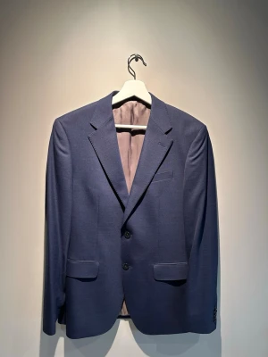 Kostym från Bläck storlek 46( Avslutning,bal,student,mm.) - Snygg blå kostymkavaj från Bläck i tailored fit. Klassisk modell med två knappar framtill, fickor med lock och bröstficka. Perfekt för dig som vill ha en stilren och modern look. Fodrad insida och diskreta detaljer.Storlek 46. Endast använd 1 gång! Nypris 3000kr. Hör av er vid frågor. MVH Viggo😁