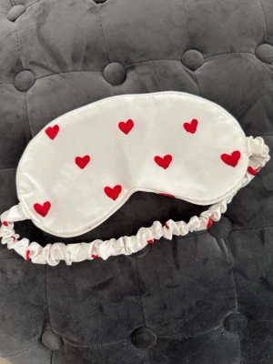 Vit sovmask med röda hjärtan - Vit sovmask i satinliknande material med röda hjärtan över hela framsidan. 