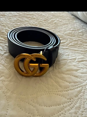 Svart  bälte med guldspänne - Snyggt svart bälte med ikoniskt dubbelt G-spänne i guld. Bältet passar perfekt för att lyfta vilken outfit som helst. Klassisk design med exklusiv känsla.