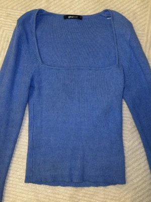 Blå ribbad topp från Gina Tricot - Trendig blå långärmad topp från Gina Tricot med fyrkantig ringning och ribbad struktur. Toppen är figurnära och har långa ärmar med slits vid ärmsluten. Perfekt att styla med jeans eller kjol för en snygg look.