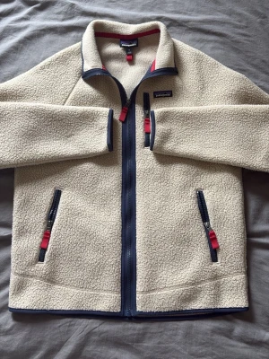 Patagonia fleece - En beige fleecejacka från Patagonia med mjukt, fluffigt material. Fleecejackans krage fungerar både som ståkrage och nervikt om man skulle vilja de. Nypris 1700kr, mitt pris 899kr