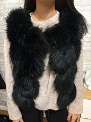Svart fluffig pälsväst - Snygg svart pälsväst med fluffig och voluminös känsla. Västen har en klassisk ärmlös design och är tillverkad i fuskpäls som ger en lyxig look. Perfekt att slänga över en tröja för att lyfta outfiten, passar dig som även bär på stolen S