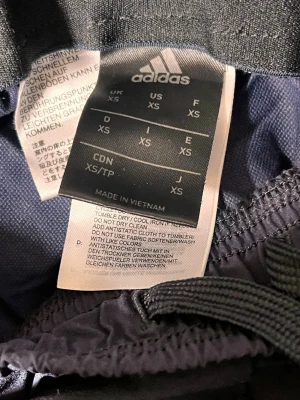 Svarta mjukisbyxor från Adidas XS - Säljer ett par svarta mjukisbyxor från Adidas i storlek XS. Byxorna har klassiska Adidas-loggan och ränder på sidan, samt dragsko i midjan för skön passform. Perfekta för chill eller träning. Tillverkade i mjukt material för extra komfort.