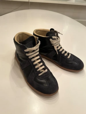 Maison Margiela High Tops GATs - Exklusiva Maison Margiela Hightops GATs i storlek 45. Skorna är gjorda av lamb och kalv skin och dem har bra skick vilket syns på bilderna. Perfekt för kalla dagar eller lite kyligare vår nätter! Köpte skorna på second hand och fick inte med lådan.  Skriv vid minsta fundering!