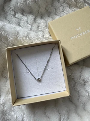 Mockberg silverhalsband med pärldetalj - Snyggt och stilrent halsband från Mockberg i silverfärgad metall. Halsbandet har en tunn kedja och en liten rund pärldetalj i mitten. Perfekt för dig som gillar minimalistiska smycken och vill ha något enkelt men elegant. Använd fåtal gånger
