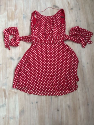50-tals inspirerade Röd prickig omlottklänning - Söt röd omlottklänning med vita prickar och knytband i midjan. Klänningen har en luftig kjol och är 50-tals inspirerad. Kostade över 1000kr egentligen och har aldrig använts 