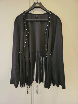 Svart cardigan med fransar och pärlor - Cool svart cardiganjacka från Shein med långa fransar nedtill och pärldetaljer längs öppningen. Jackan har en öppen modell och vida ärmar, vilket ger en avslappnad och trendig look. Perfekt för att lyfta vilken outfit som helst. Stl xxl