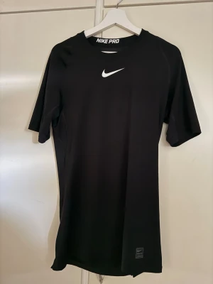 Svart Nike Pro Dri-fit träningströja - Säljer en svart Nike Pro träningströja med vit logga på bröstet. T-shirten har korta ärmar, rund halsringning och är tillverkad i ett stretchigt funktionsmaterial som andas. Perfekt för gymmet eller löpning.