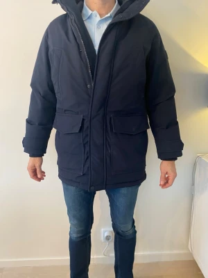 Marinblå jacka från Tommy Hilfiger - Hej! Säljer nu min riktigt snygga och stilrena jacka ifrån märket Tommy Hilfiger. Jackan är använd ett fåtal gånger och är därför i mycket bra skick. Jackan är lite längre i modellen. Modellen heter ”Rockie Down - parkas”.Jag säljer den till ett riktigt bra pris. Ny pris på jackan är 4500. Mitt pris är 1600