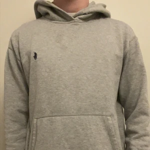 Grå hoodie från Polo Ralph Lauren - Klassisk grå hoodie från Polo Ralph Lauren med broderad logga på bröstet. Hoodien har huva, känguruficka och är tillverkad i mjukt bomullsmaterial. Perfekt för en avslappnad och stilren look. Den är i M men passar även s, inga defekter förutom att snörena inte är kvar💫