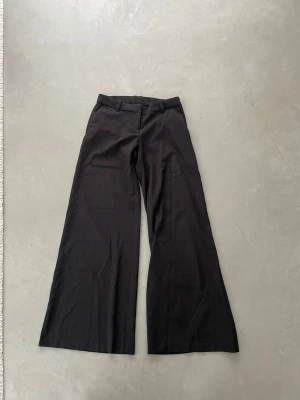 Svarta kostymbyxor från Weekday - Snygga svarta kostymbyxor från Weekday med vida ben och låg midja. Klassisk design med hällor för skärp och diskret dragkedja framtill. Perfekta för en clean och stilren look. Tillverkade i ett mjukt och följsamt tyg.