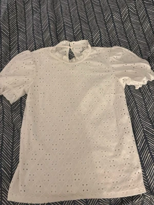 Vit spetsblus med puffärm från Vila - Söt vit blus från Vila med puffärmar och broderade spetsdetaljer. Blusen har rund halsringning och knapp i nacken. Perfekt för dig som gillar romantisk och feminin stil.