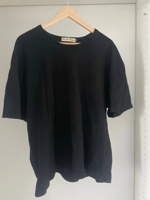 Svart basic t-shirt från The Blue Uniform - En klassisk svart t-shirt från The Blue Uniform med rund hals och avslappnad passform. Tillverkad i mjuk bomull, perfekt för en enkel och stilren look. Passar till allt och är ett måste i garderoben.