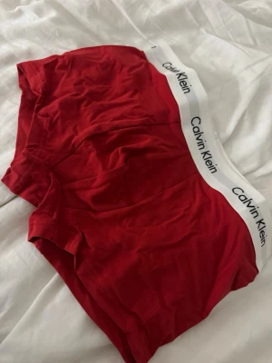 Tre pack kalsonger Calvin Klein - Säljer ett tre pack kalsonger från Calvin Klein, ena paret är rött, det andra mörkblått och ett vitt. Båda har vit resår med klassisk Calvin Klein-logga. Sköna och stilrena boxermodeller i mjukt material, perfekta för vardagsbruk.