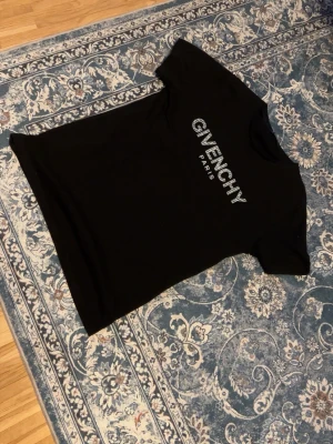 Svart Givenchy t-shirt med logga - Snygg svart t-shirt från Givenchy med stor vit logga och texten PARIS på bröstet. T-shirten har klassisk passform och korta ärmar. Perfekt för dig som vill ha en stilren och trendig look med exklusiv känsla.