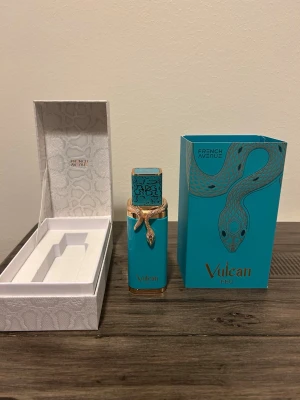 Vulcan Feu parfym från French Avenue - Unik parfym i turkos flaska med gulddetaljer och ormdekor från French Avenue. Flaskan har en fyrkantig form och levereras i en elegant vit ask med ormmönster samt matchande turkos kartong med ormtryck. Perfekt för dig som gillar exklusiv design.