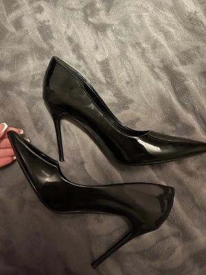 Svarta lackpumps med spetsig tå - Snygga svarta pumps i lack med spetsig tå och hög smal klack. Klassisk och elegant modell som ger en stilren look. Perfekta för att lyfta vilken outfit som helst.