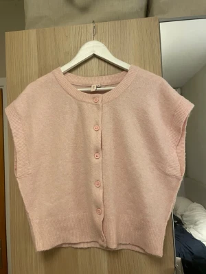 Ljusrosa stickad väst från Nelly - Supersöt ljusrosa stickad väst från Nelly med rund halsringning och knappar framtill. Västen har ribbade kanter och är ärmlös, perfekt att styla över en skjorta eller t-shirt. Mjuk och skön känsla, passar dig som gillar en avslappnad men trendig look.